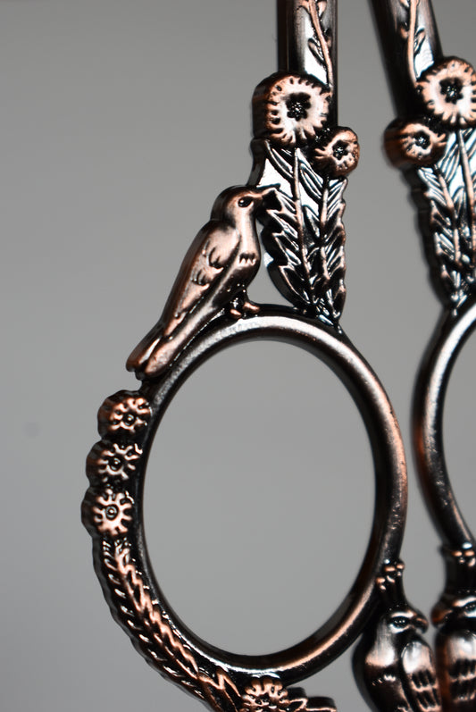 Decorative bronze yarn scissors with intricate bird and flower designs.
