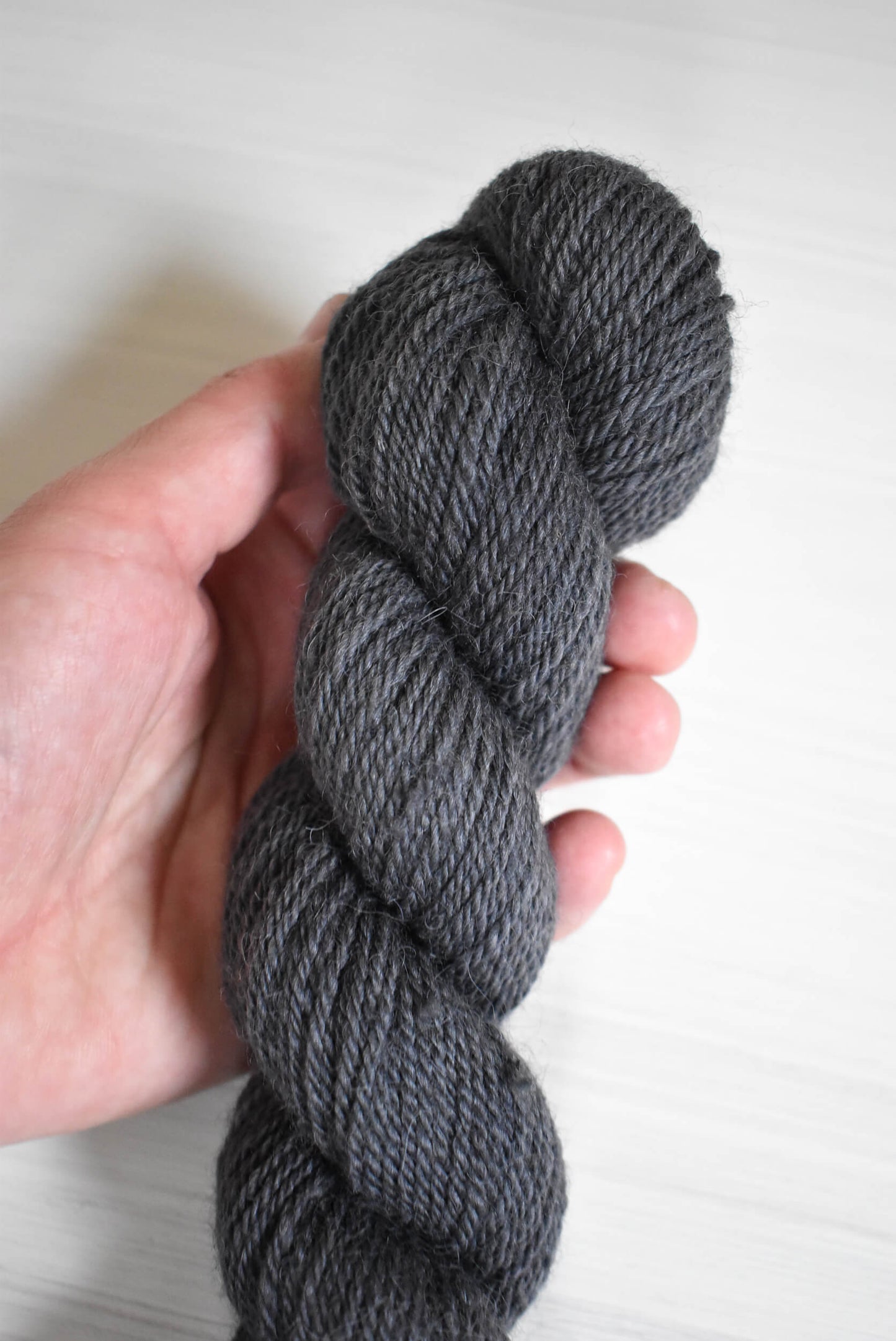 Gray skein of navy blue yarn held in a hand.