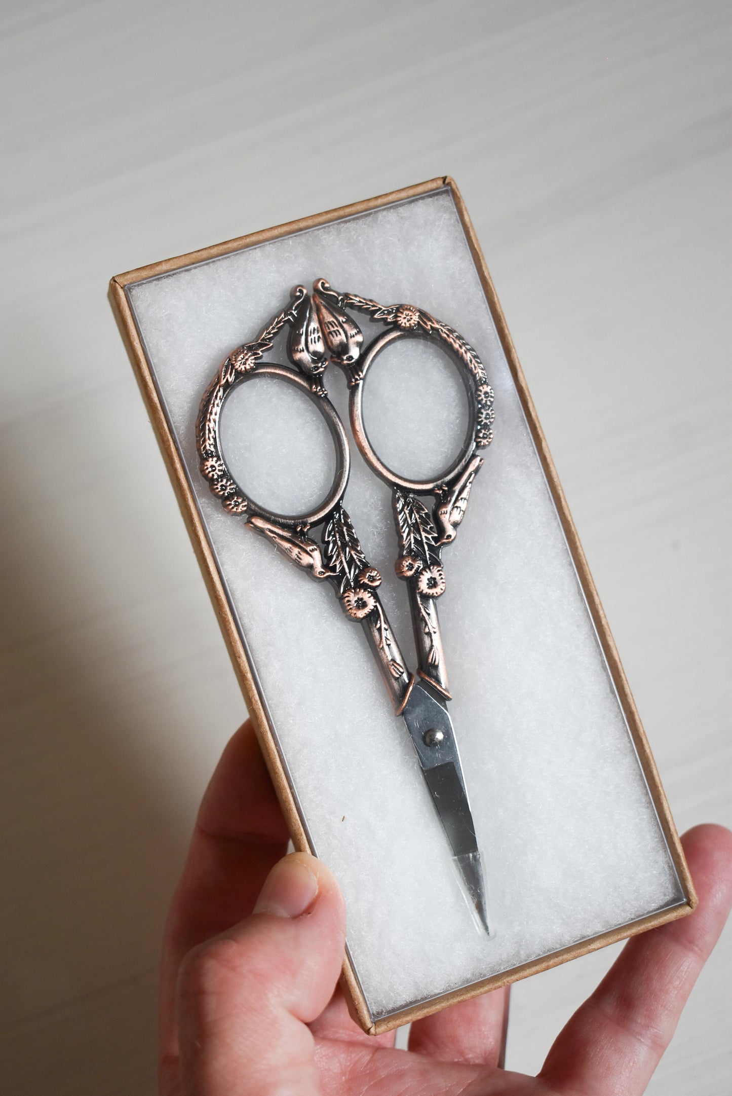 Decorative yarn scissors in a box held by a hand against a neutral background.
