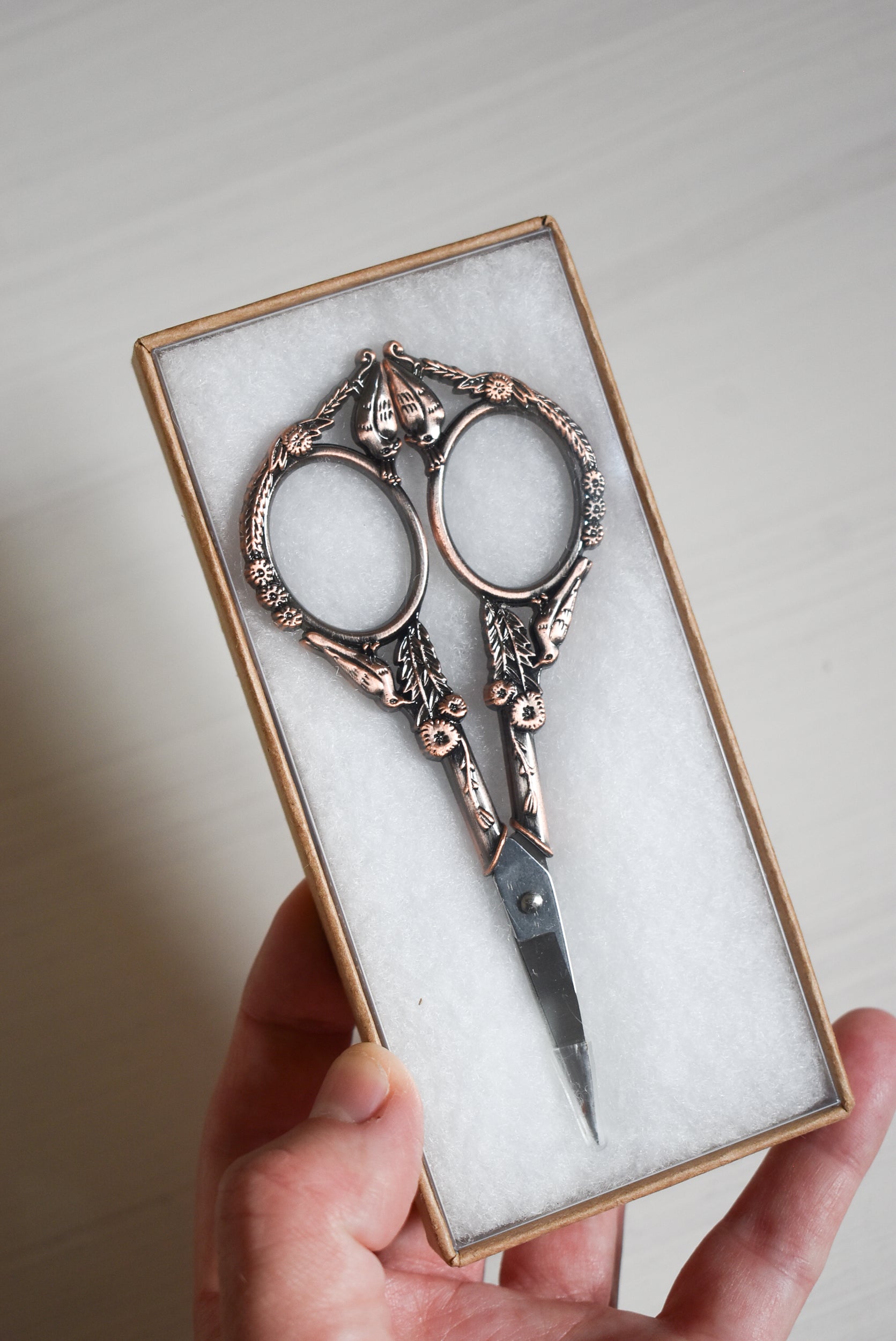 Decorative yarn scissors in a box held by a hand against a neutral background.