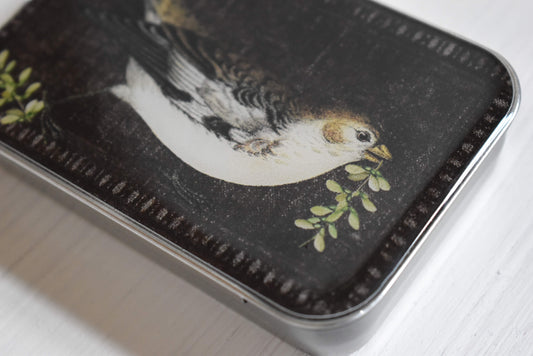 Detail of the knitting notions tin with a bird design on a dark background.