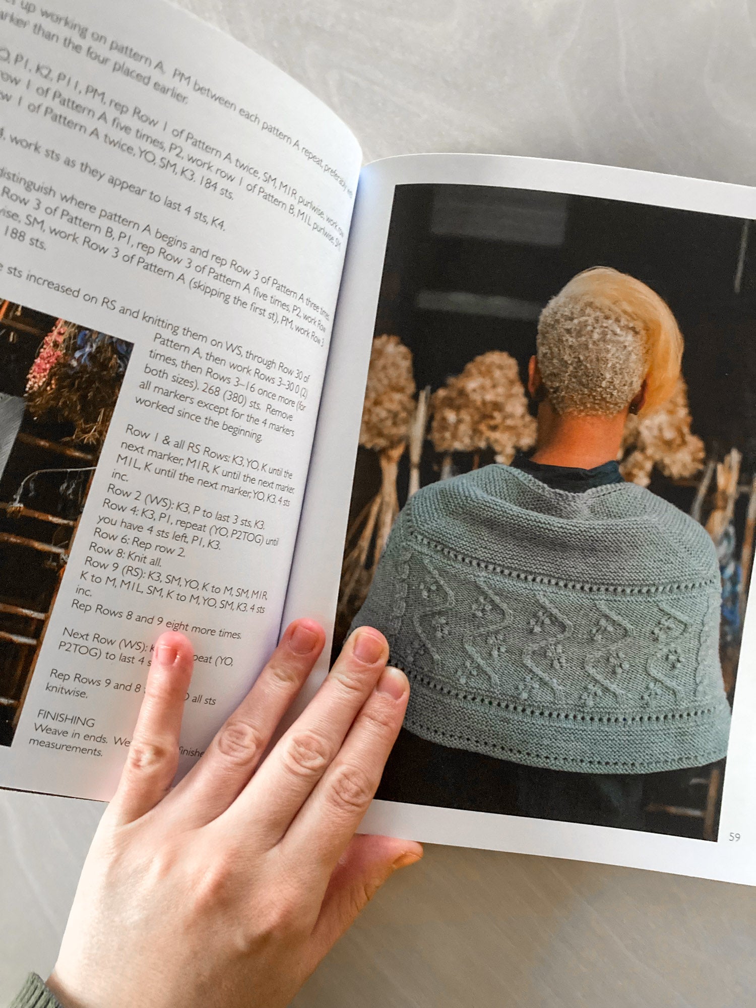 Open book showing a pattern for a knitted shawl with a person wearing it, held open by a hand.