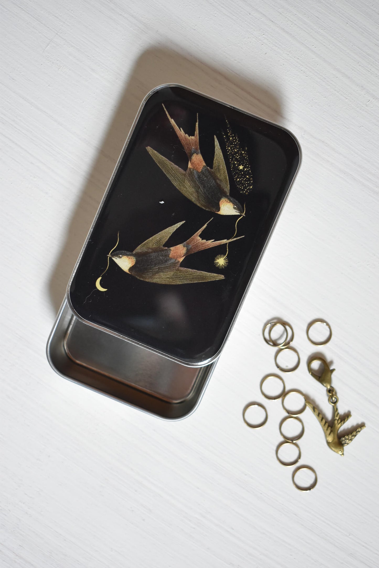Knitting notions tin with a black cover design showing two swallows.