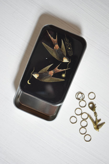 Knitting notions tin with a black cover design showing two swallows.