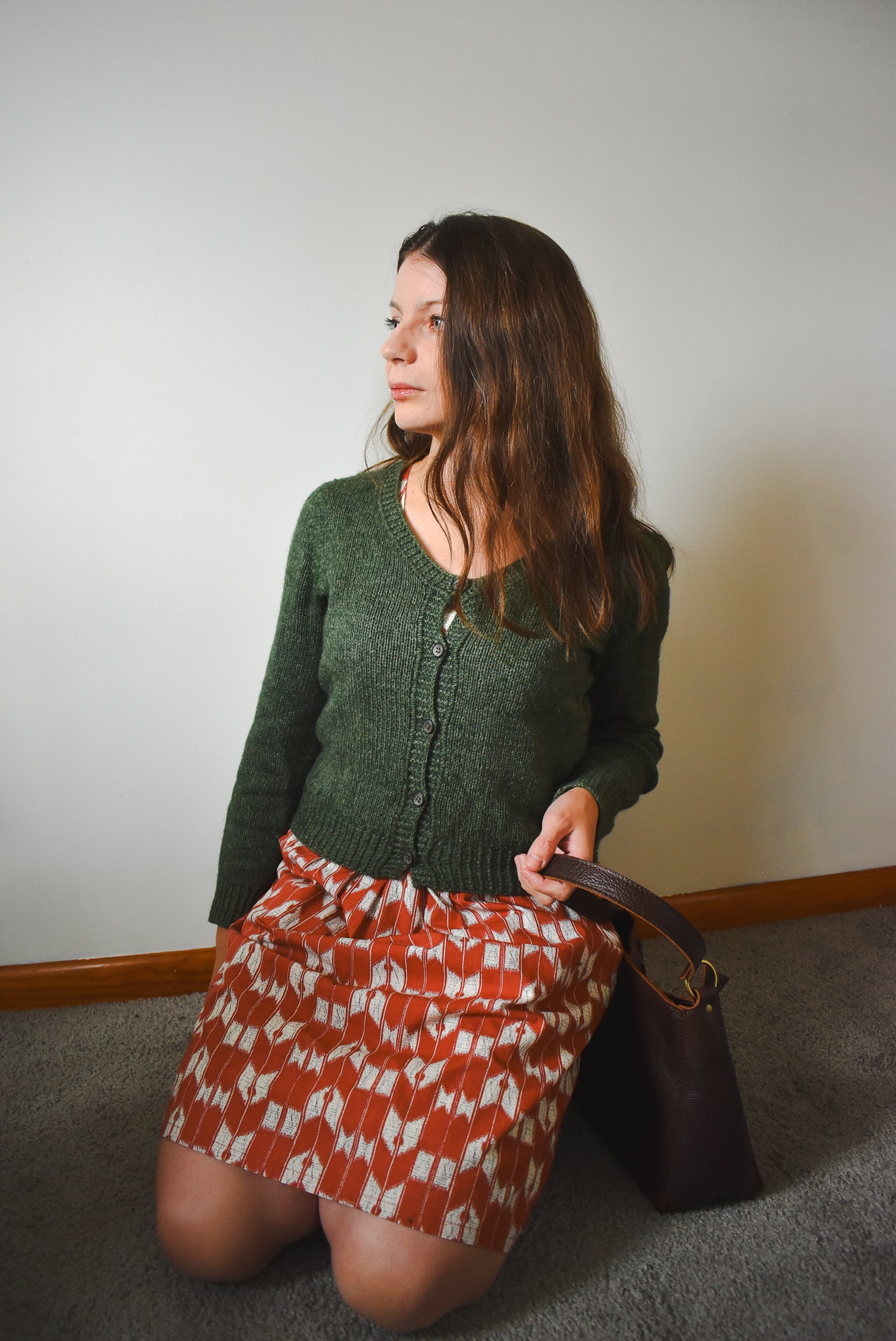 Woman wearing a green cardigan and patterned dress, holding a brown handbag.