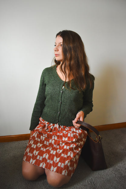 Woman wearing a green cardigan and patterned dress, holding a brown handbag.
