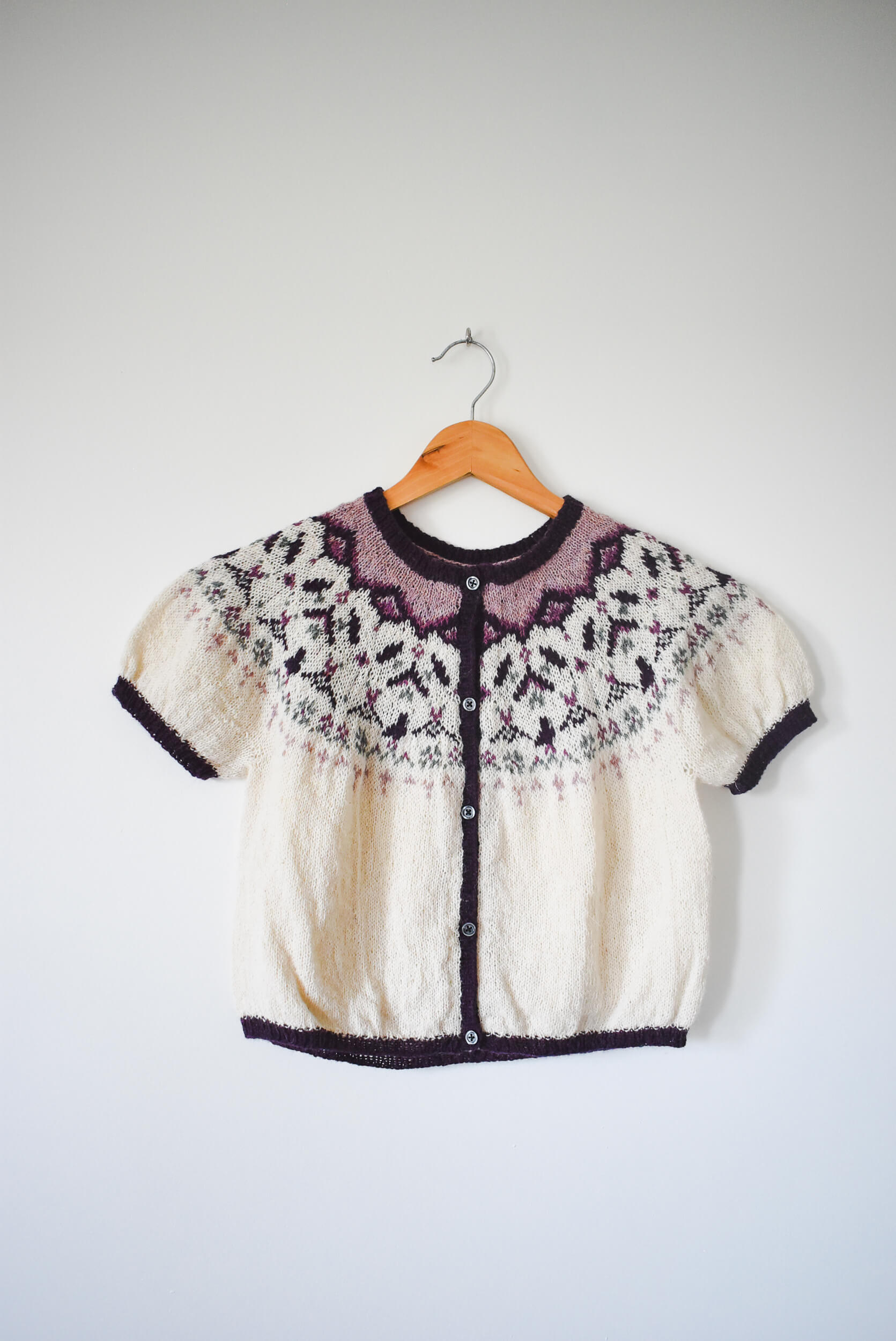 Knitted sweater with a floral pattern featuring birds and botanical motifs.
