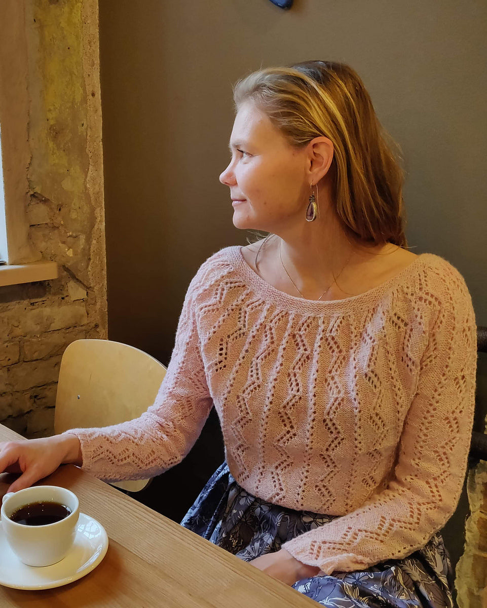 Woman sitting at a table with a cup of coffee, wearing her finished hand-knit Battenkill Pullover.
