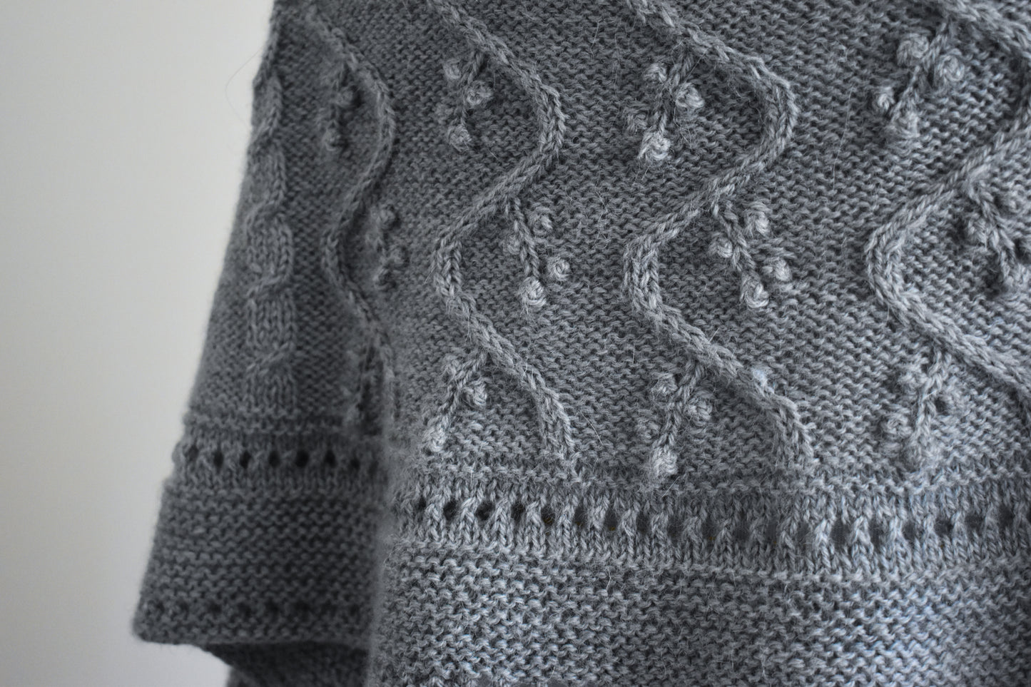 Close-up of a gray knitted fabric with intricate patterns on a plain background