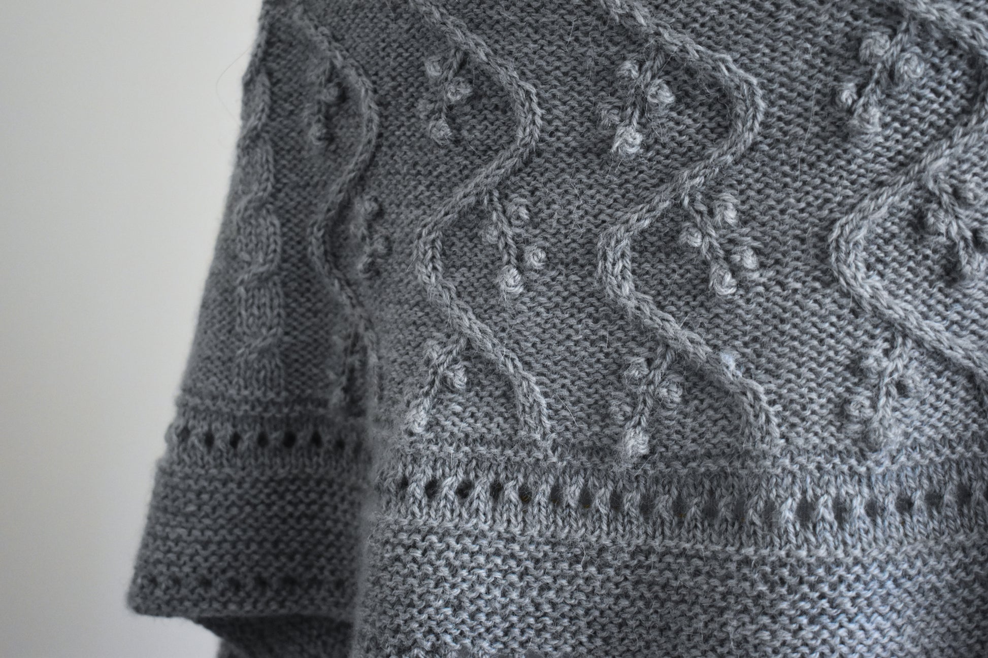 Close-up of a gray knitted fabric with intricate patterns on a plain background