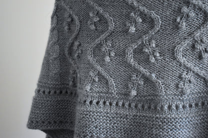 Close-up of a gray knitted fabric with intricate patterns on a plain background
