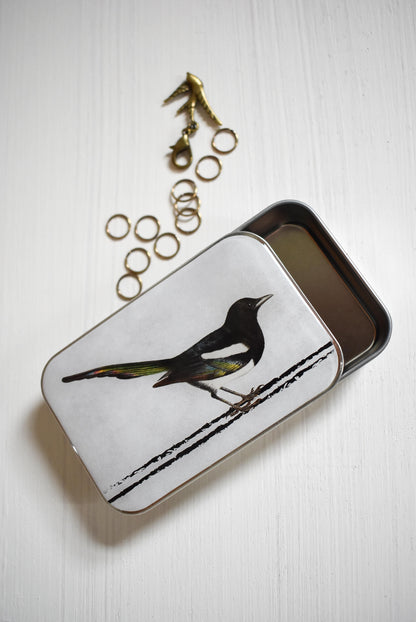 The special limited-edition slider knitting notions tin features a vintage-inspired illustration of a magpie.