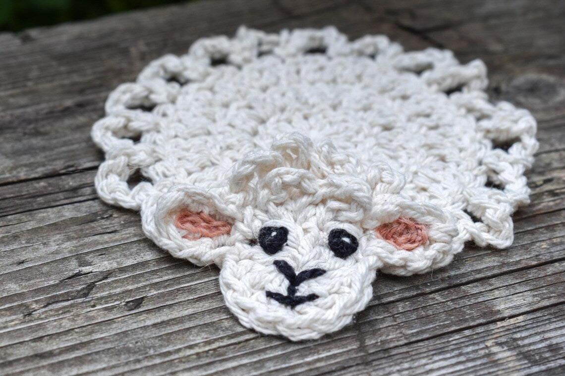 Crocheted sheep coaster on a wooden surface.