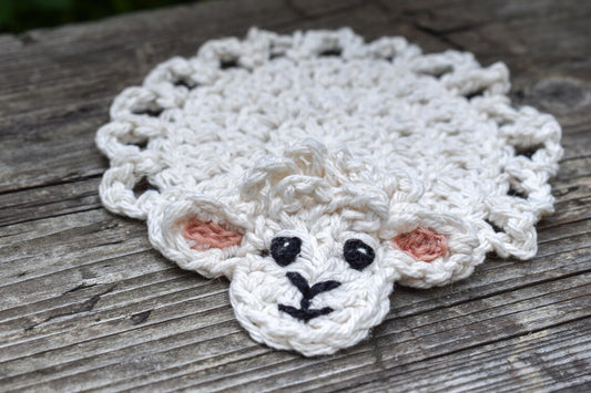 Crocheted sheep coaster on a wooden surface.