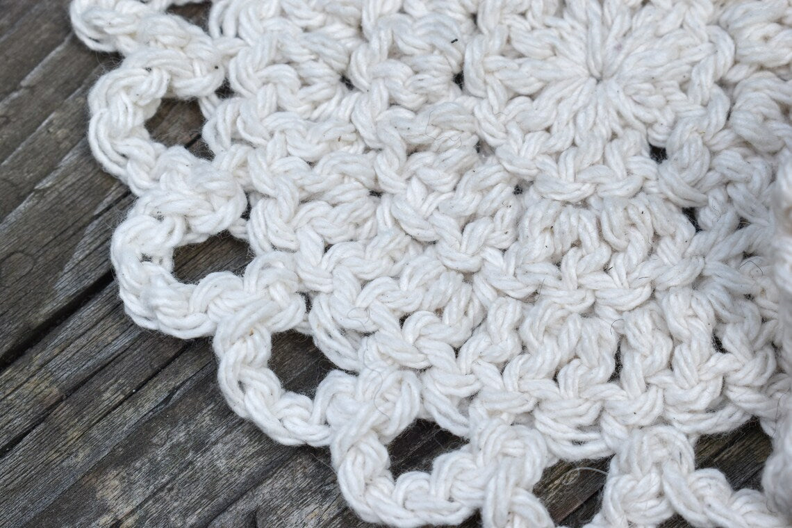 Close-up of a white crocheted coaster on a wooden surface.