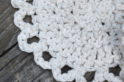 Close-up of a white crocheted coaster on a wooden surface.