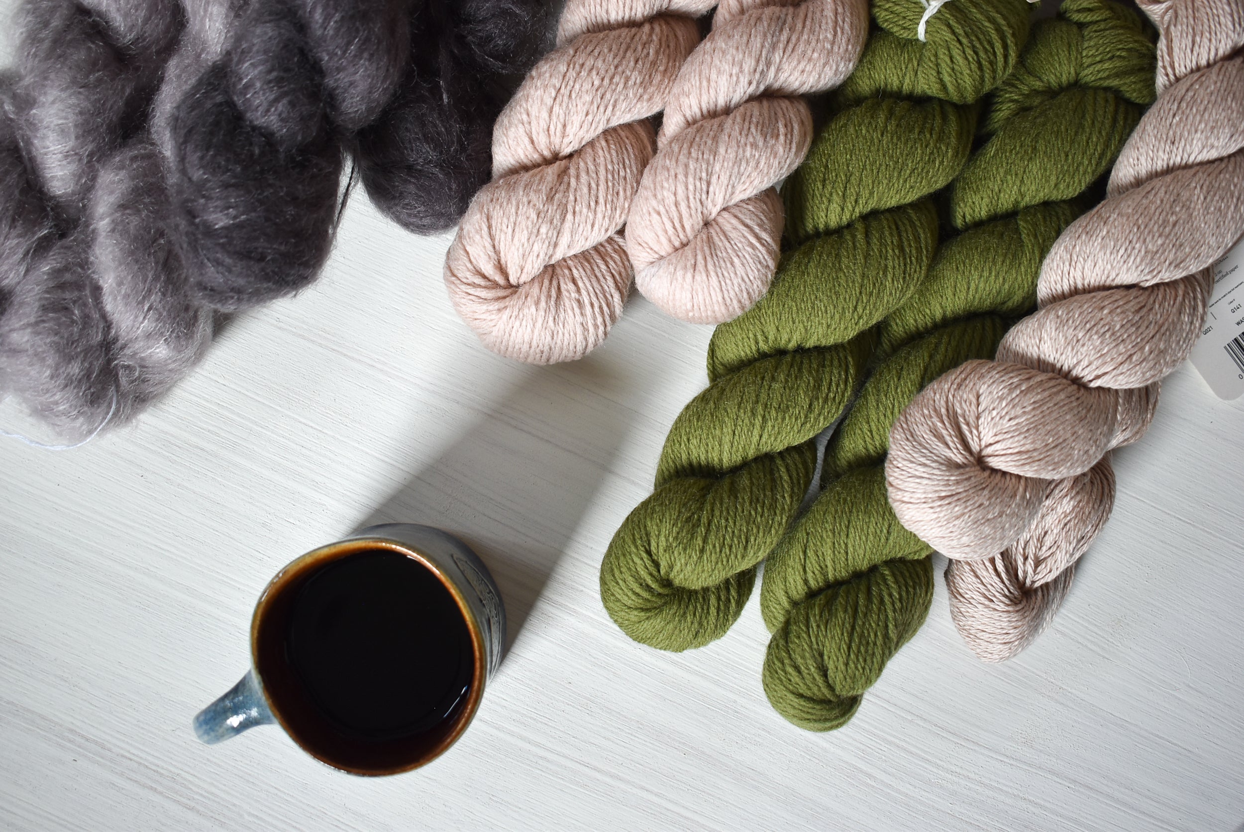 Yarn skeins in various spring colors on a white surface with a mug, showing products Nest Creative Works modern yarn and knitting supplies shop.
