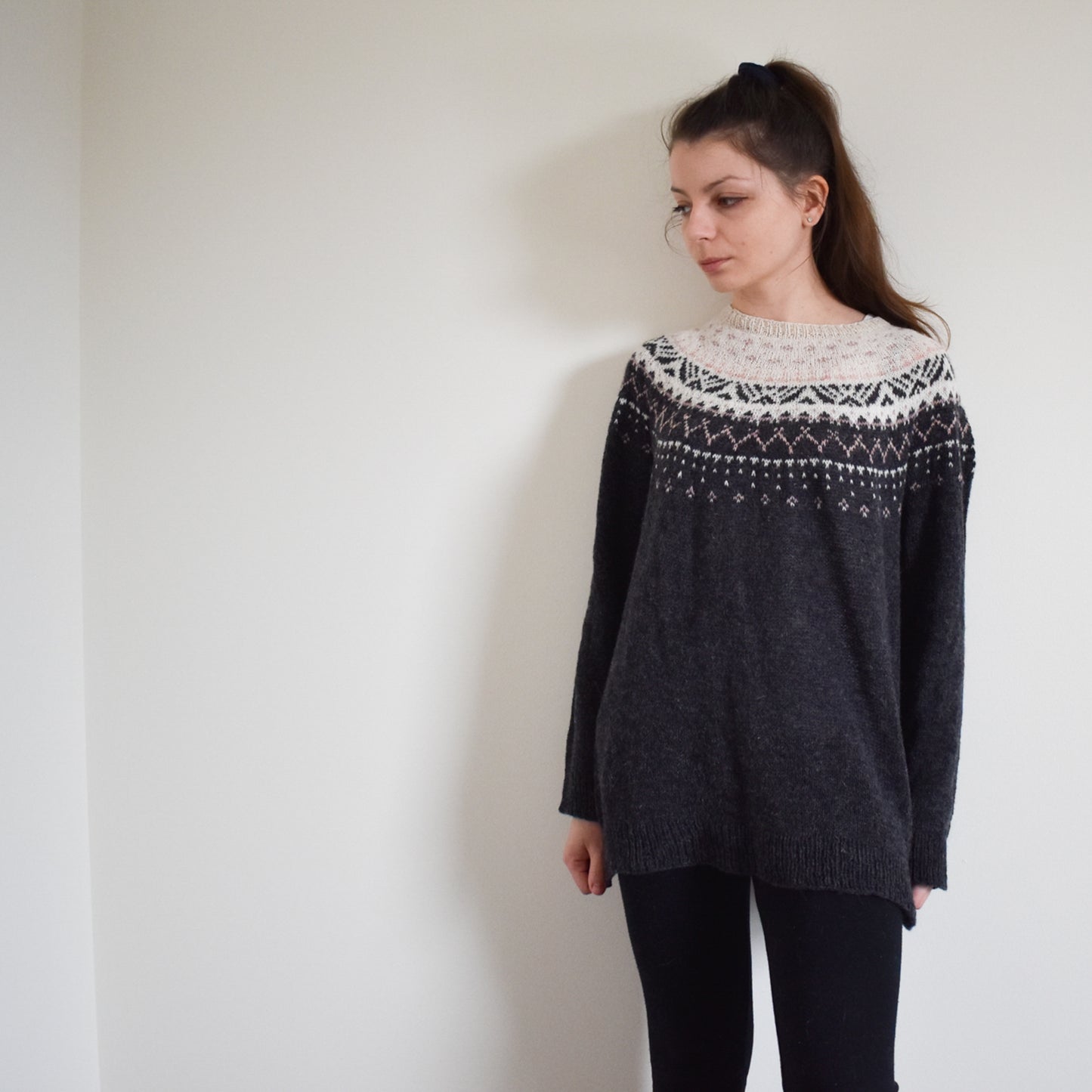 Woman wearing a dark gray and pink jacquard sweater.