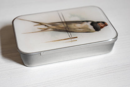 Rectangular knitting notions tin box with a swallow bird design on a white wooden surface.