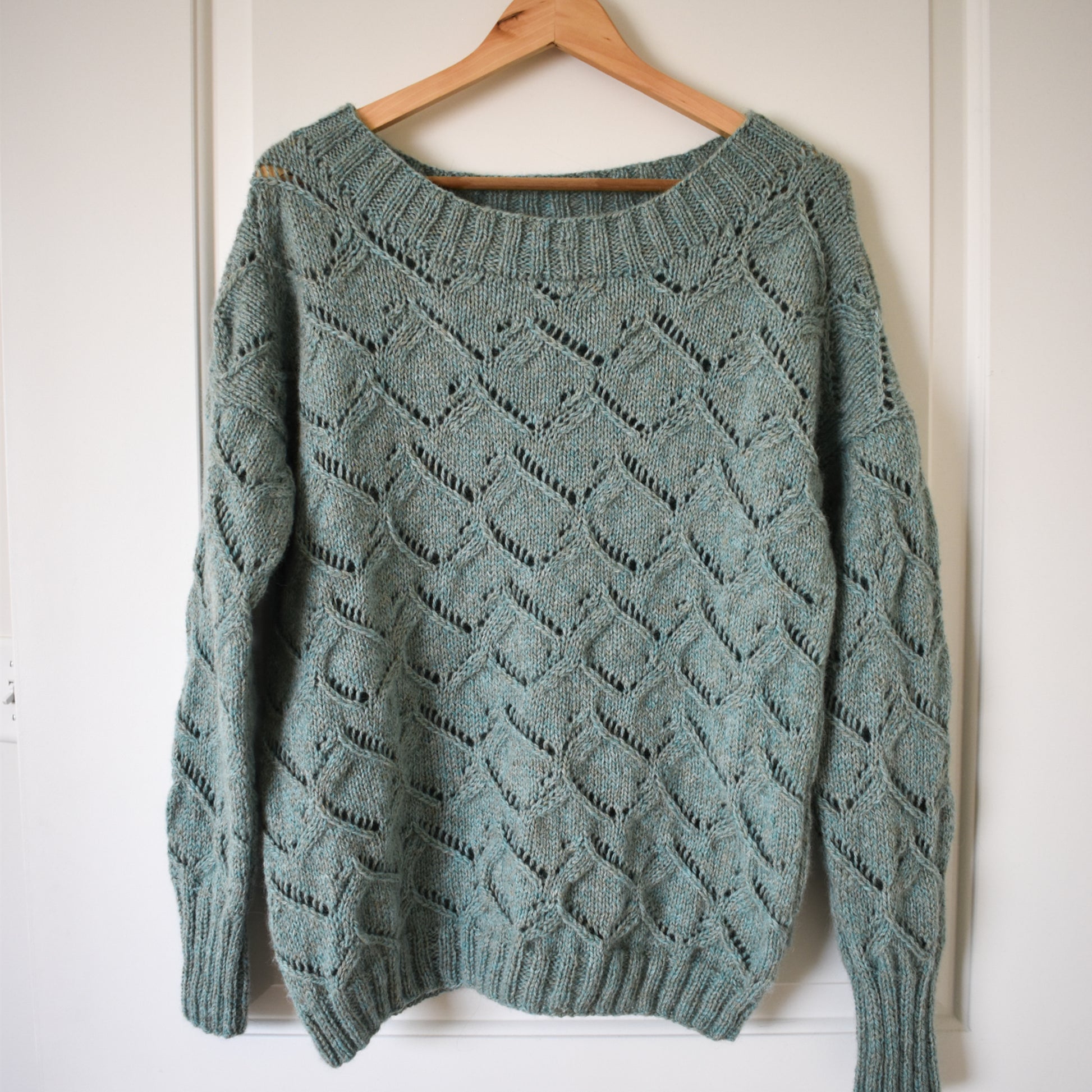 A photo of the Waterspaces Pullover knitting pattern, showing the finished sweater on a wooden hanger.
