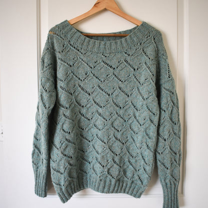 A photo of the Waterspaces Pullover knitting pattern, showing the finished sweater on a wooden hanger.