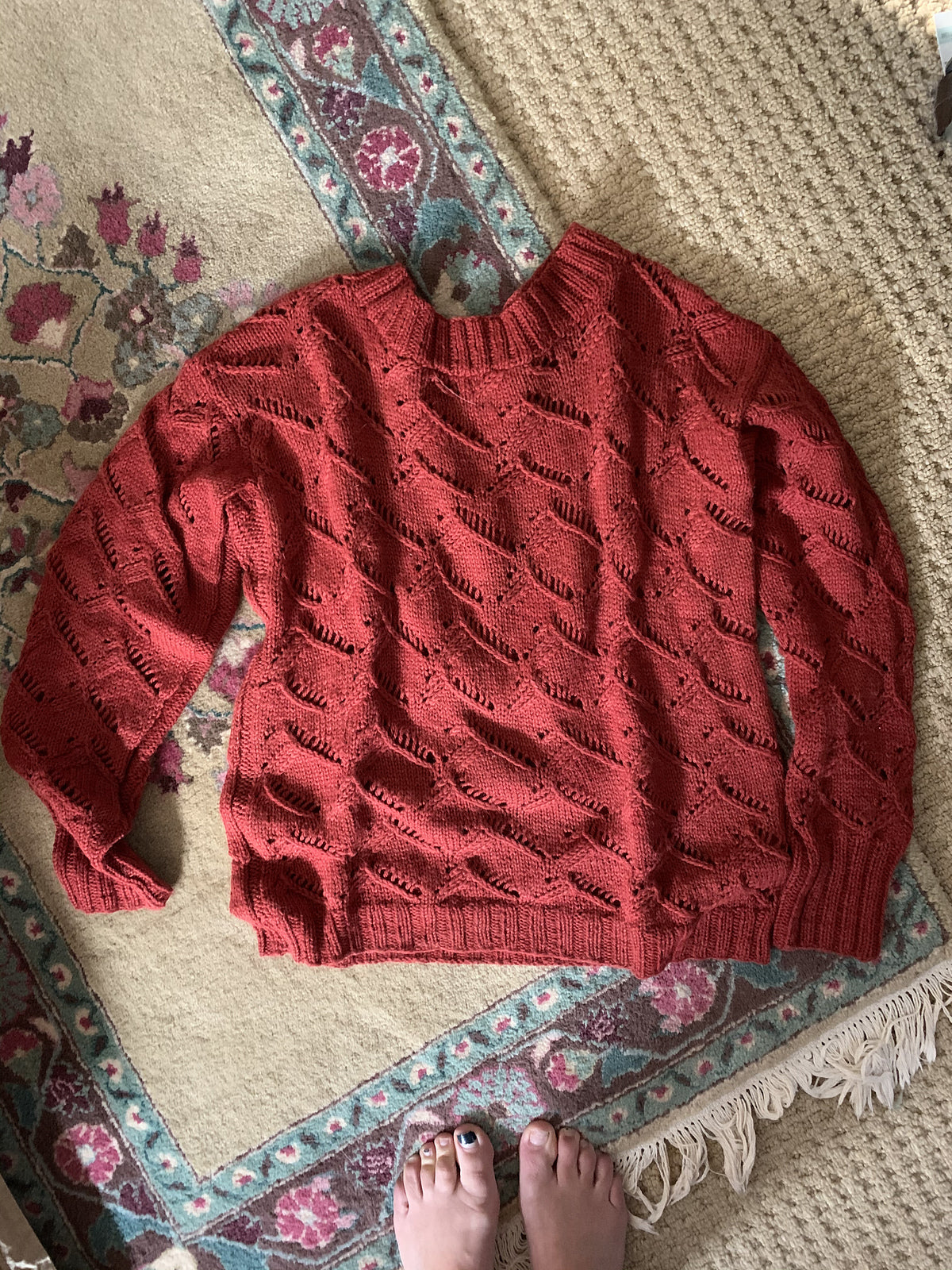 A photo of a red sweater on a patterned rug, based on the Waterscapes Pullover pattern.