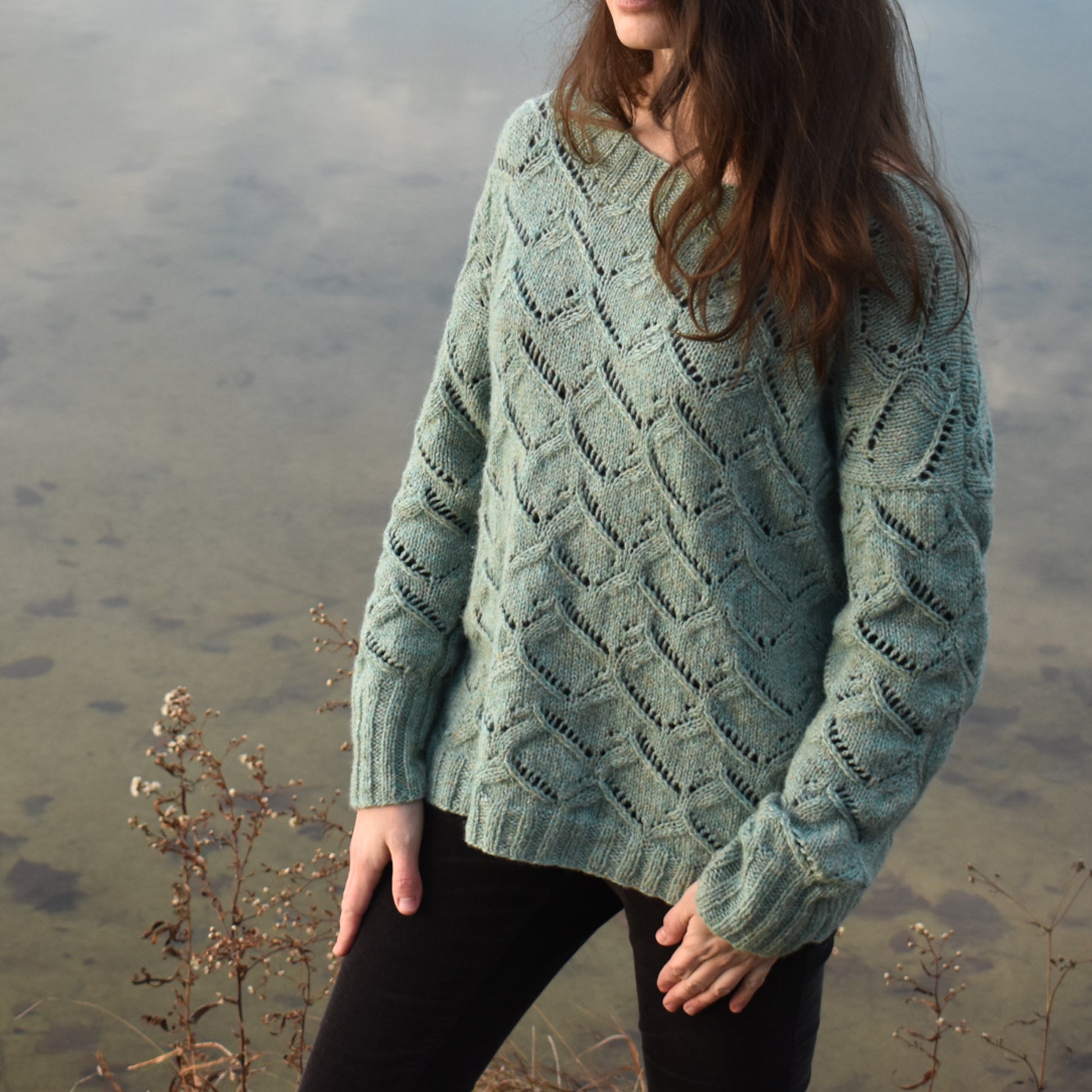 Person wearing a textured green sweater, the Waterscapes pullover, standing by a body of water.