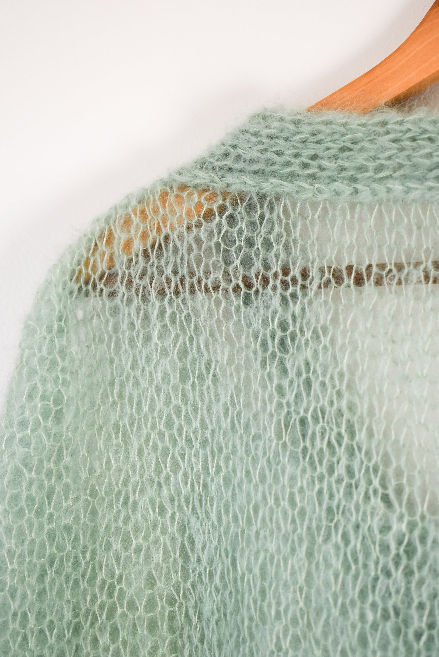 A close-up of a light sage green open-knit mohair blouse knitting pattern.