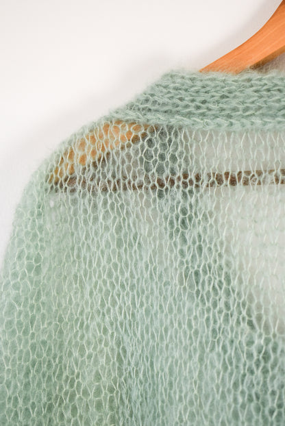 A close-up of a light sage green open-knit mohair blouse knitting pattern.