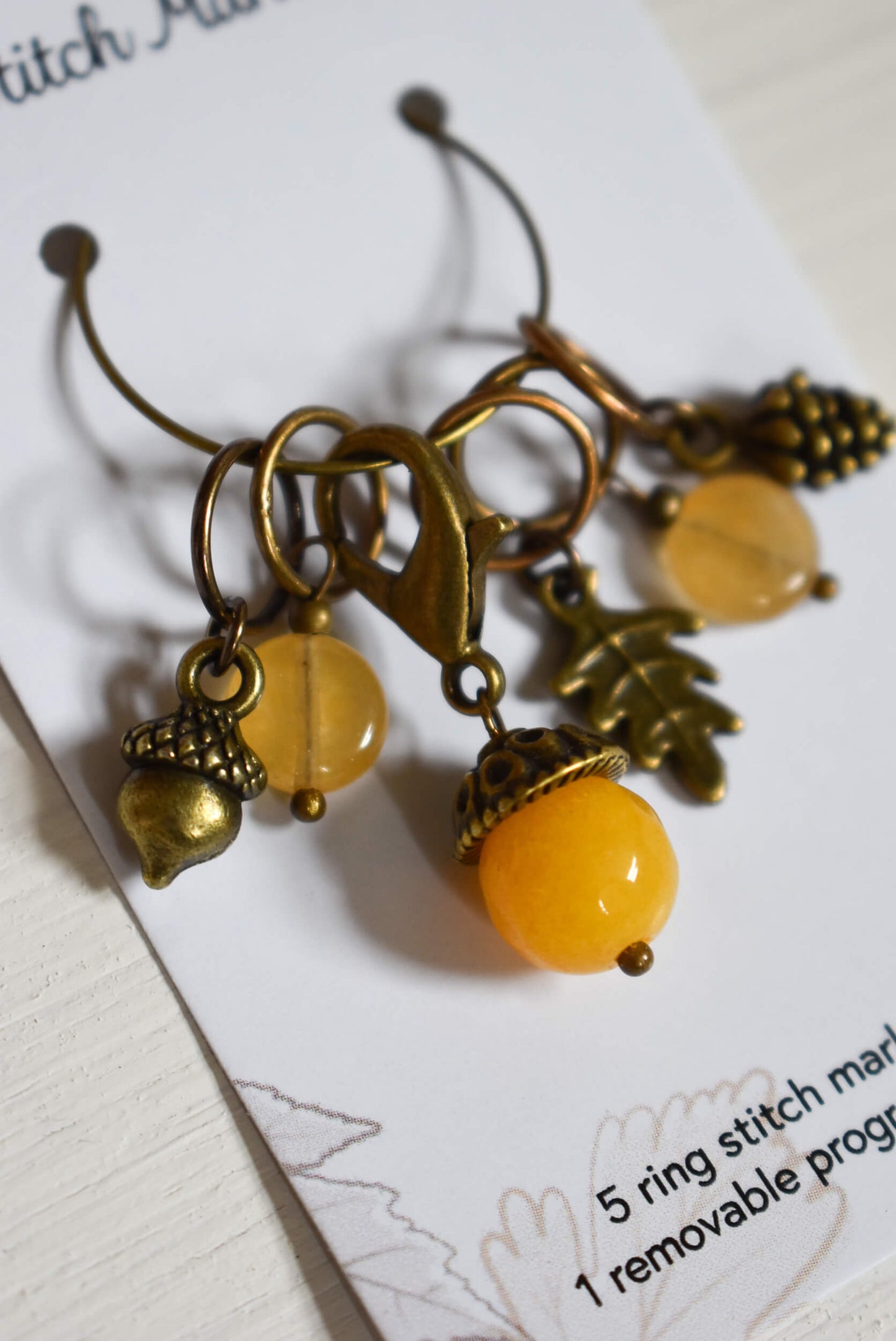 Decorative stitch markers with yellow beads and acorn charms.